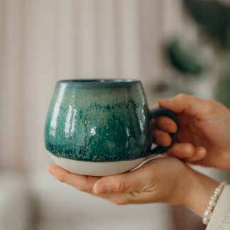 Grüne Tasse mit beigen Streifen unten wir von einer Person in den Händen gehalten